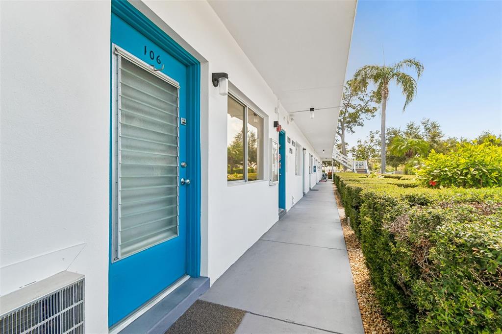 An exterior walkway leads past blue doors of motel-style rooms with a hedge alongside — 8220 112TH STREET UNIT 106, SEMINOLE, FL