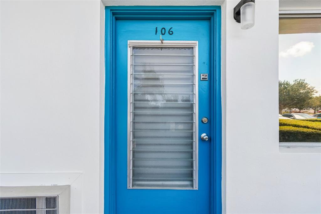 A bright blue exterior door with a louvered glass window insert and the number 106 — 8220 112TH STREET UNIT 106, SEMINOLE, FL