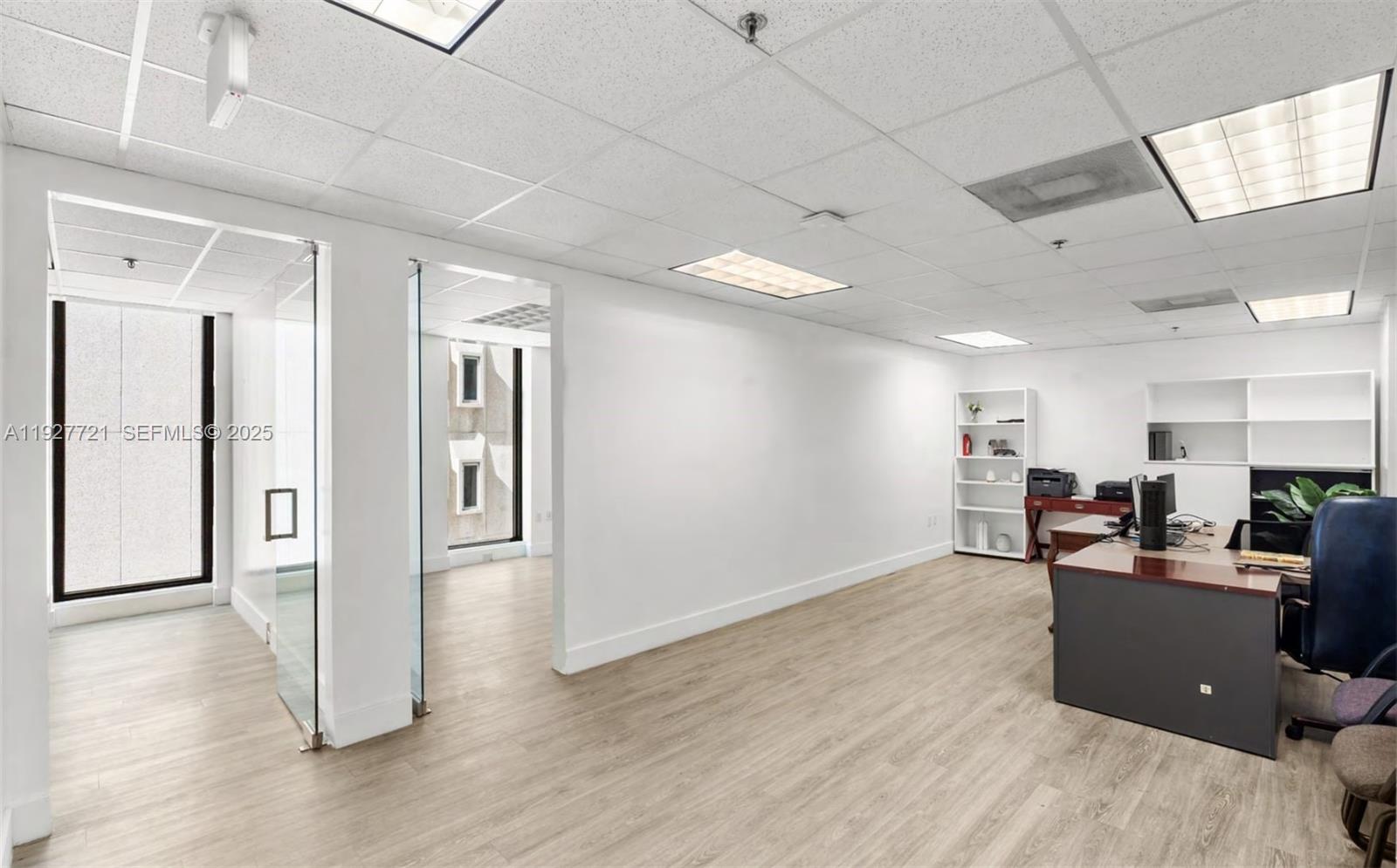 An office space features white walls, light wood flooring, glass partitions, and a desk area — 66 W FLAGLER ST # 502, Miami FL 33130, MIAMI, FL