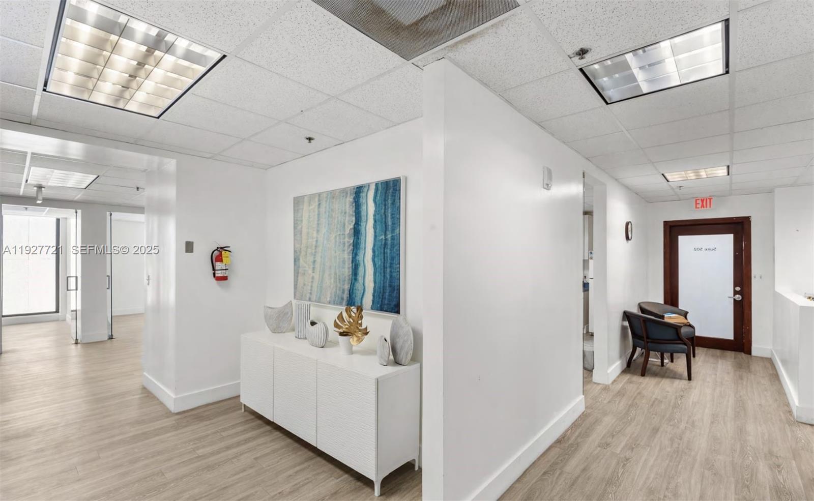 A bright office hallway features white walls, wood-look flooring, a console table, and lighting — 66 W FLAGLER ST # 502, Miami FL 33130, MIAMI, FL