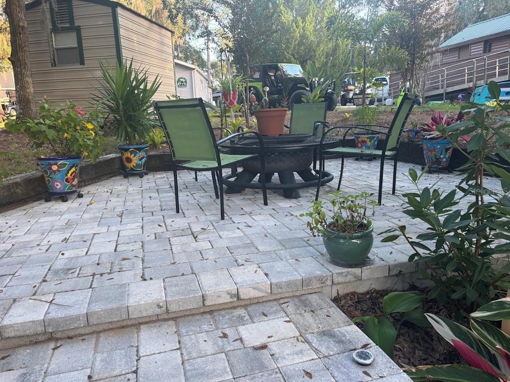 A paved patio features a fire pit, outdoor chairs, and various potted plants — 25244 NE 143RD  ST UNIT 180, SALT SPRINGS, FL
