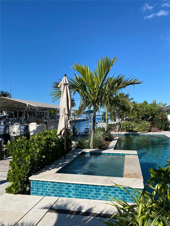 A turquoise-tiled spa sits beside a swimming pool overlooking a canal with docked boats — 3708 ROYAL PALM DRIVE, BRADENTON, FL