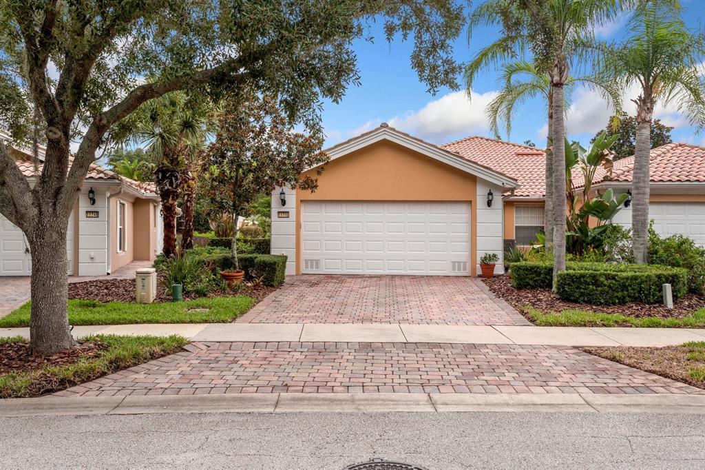 A single-story house with a white garage door, tan stucco walls, and a brick driveway — 11740 ASTILBE DRIVE, ORLANDO, FL