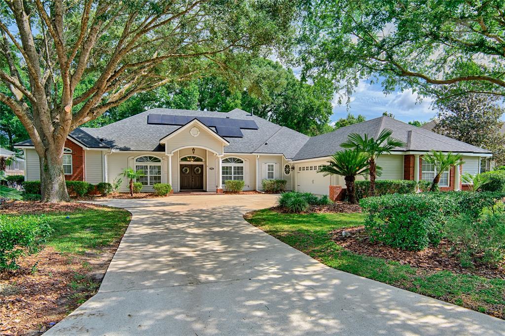 A single-story house with a concrete driveway, solar panels, and large trees in the yard — 9244 SW 31ST PLACE, GAINESVILLE, FL