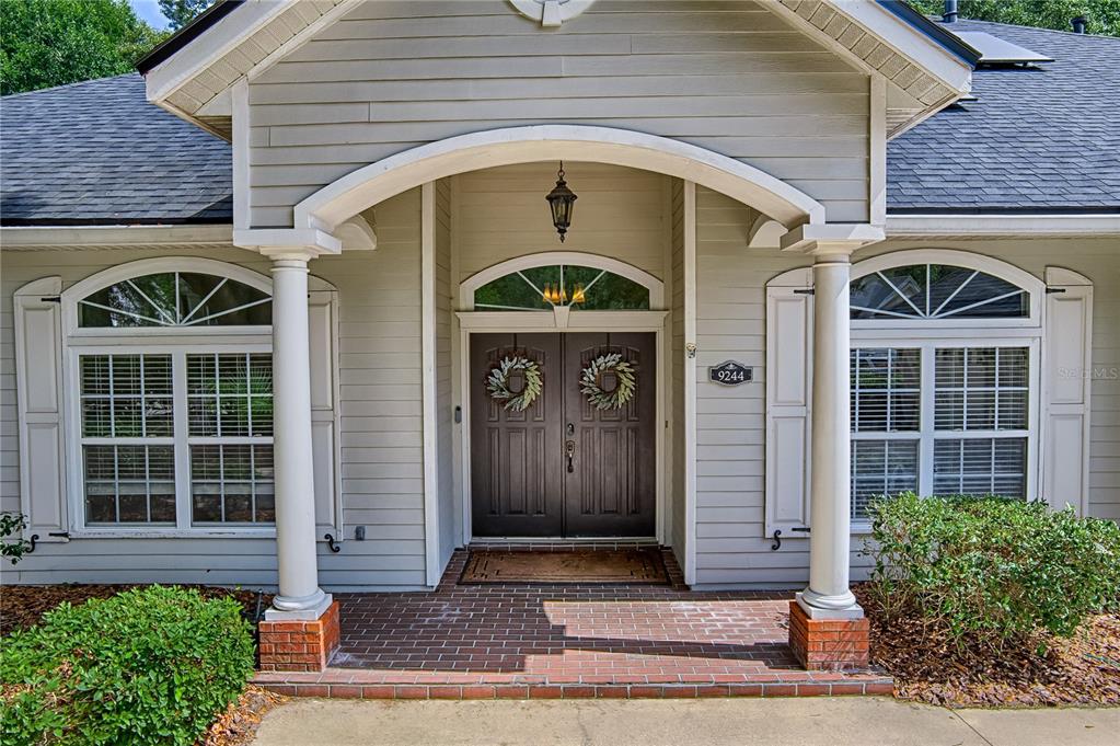The front exterior of a house features a brick porch, double doors, and two columns — 9244 SW 31ST PLACE, GAINESVILLE, FL