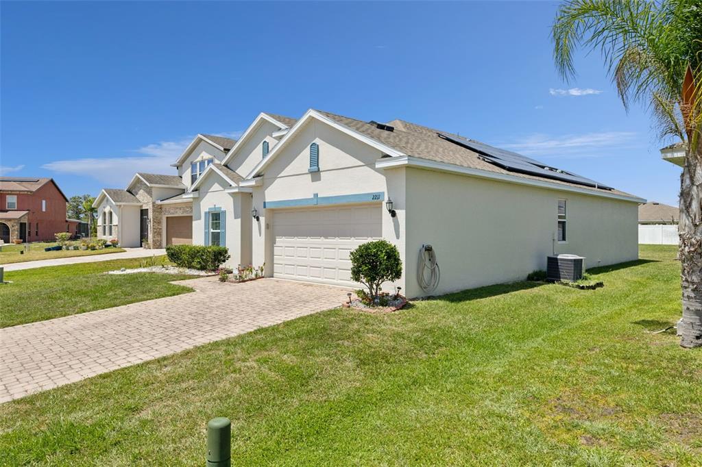 A beige suburban house with a two-car garage, solar panels, and a paved driveway — 2211 RIVERGLEN COURT, KISSIMMEE, FL