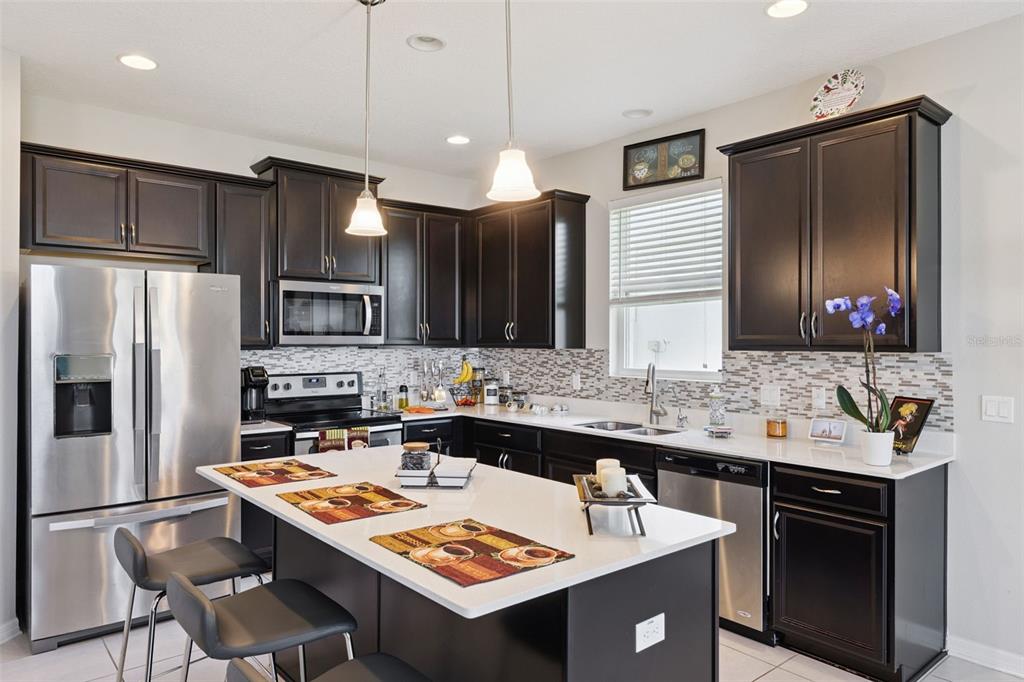 A kitchen features dark wood cabinets, stainless steel appliances, a white island, and tile backsplash — 2211 RIVERGLEN COURT, KISSIMMEE, FL