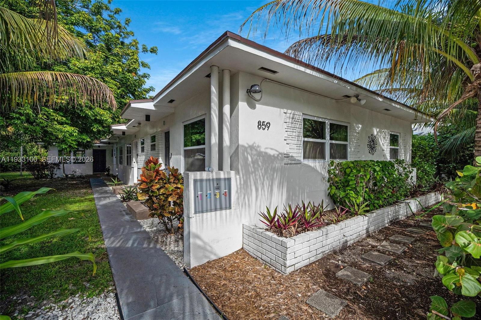 A white single-story apartment building features a walkway, a brick planter, and numbered mailboxes — 859 NE 90th St, Miami FL 33138, MIAMI, FL