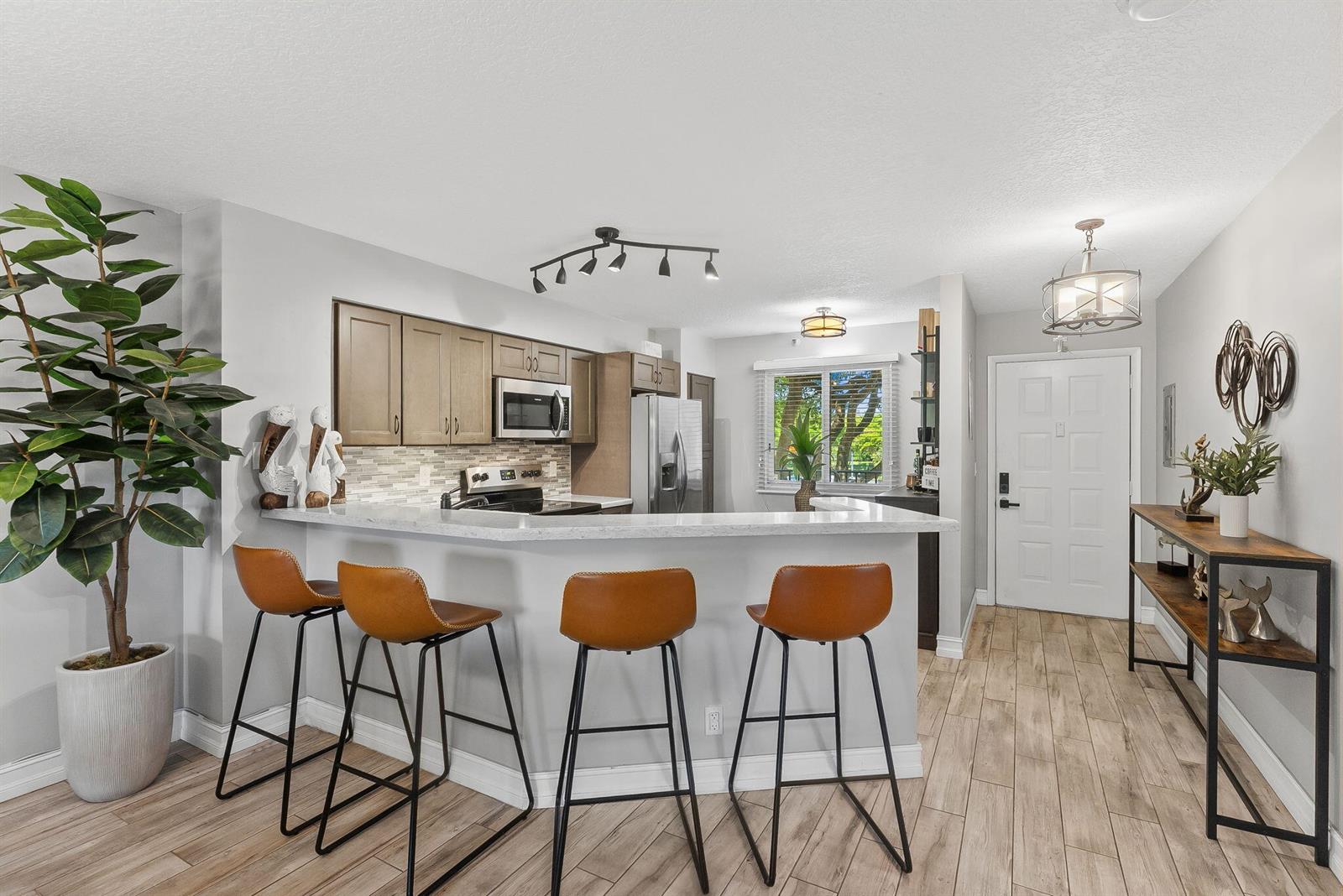 A kitchen features a breakfast bar with four stools, light wood flooring, and stainless appliances — 2215 Cypress Island Drive # 301, Pompano Beach FL 33069, POMPANO BEACH, FL