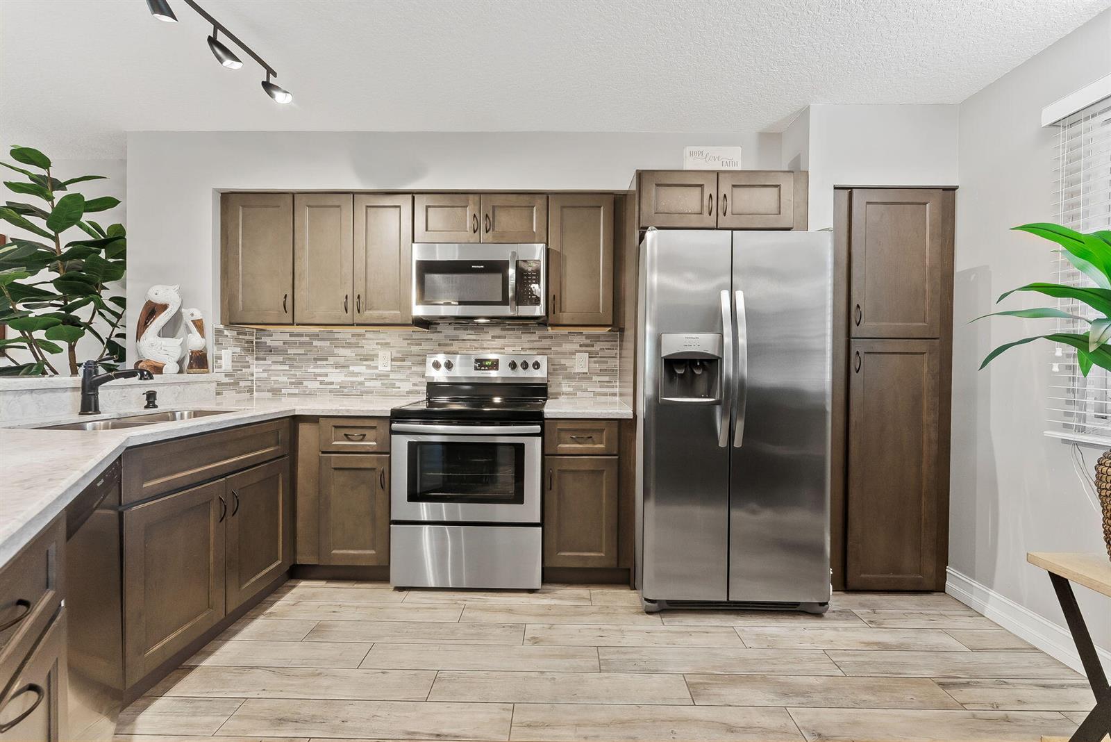 A kitchen with brown cabinets, stainless steel appliances, and light-colored wood-look tile flooring — 2215 Cypress Island Drive # 301, Pompano Beach FL 33069, POMPANO BEACH, FL