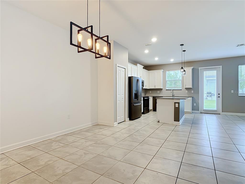 A kitchen and dining area with tile flooring, white cabinets, and a modern light fixture — 2920 TITLE STREET, KISSIMMEE, FL