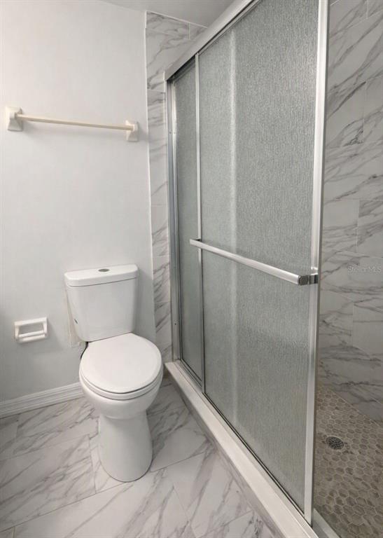 A bathroom features a white toilet, a glass-enclosed shower, and white marble-patterned tile flooring — 1412 PORTOBELLO DRIVE, PORT ORANGE, FL