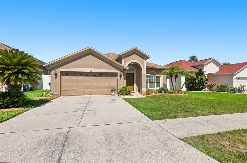 A single-story suburban house with a tan stucco exterior, two-car garage, and a front lawn — 514 GREG STREET, VALRICO, FL
