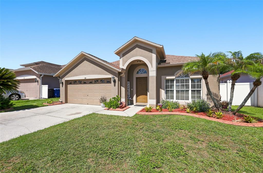 A single-story suburban house with a tan stucco exterior, a two-car garage, and palm trees — 514 GREG STREET, VALRICO, FL