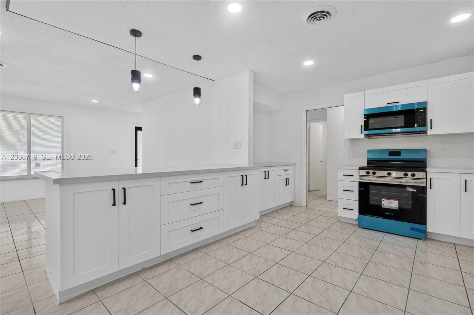 A bright kitchen features white cabinetry, a central island, and stainless steel appliances — 258 SW 8th St, Dania Beach FL 33004, DANIA BEACH, FL