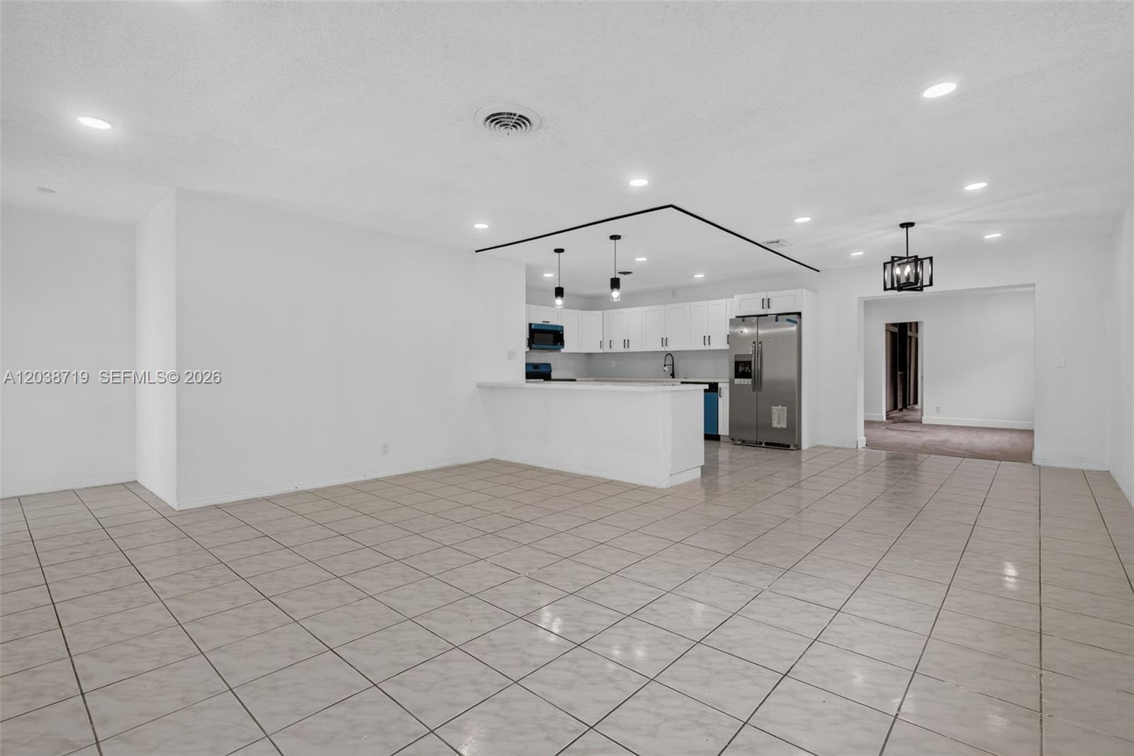An open-concept kitchen with white cabinets and a breakfast bar overlooks a tiled living area — 258 SW 8th St, Dania Beach FL 33004, DANIA BEACH, FL