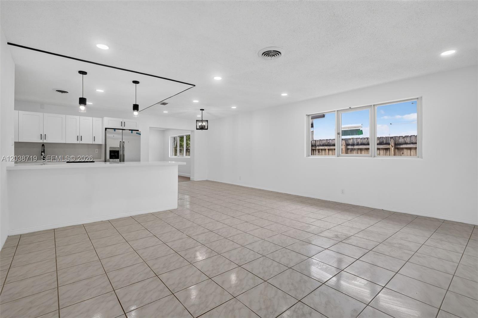 A bright, open-concept kitchen and living area featuring white cabinets, tile flooring, and recessed lighting — 258 SW 8th St, Dania Beach FL 33004, DANIA BEACH, FL