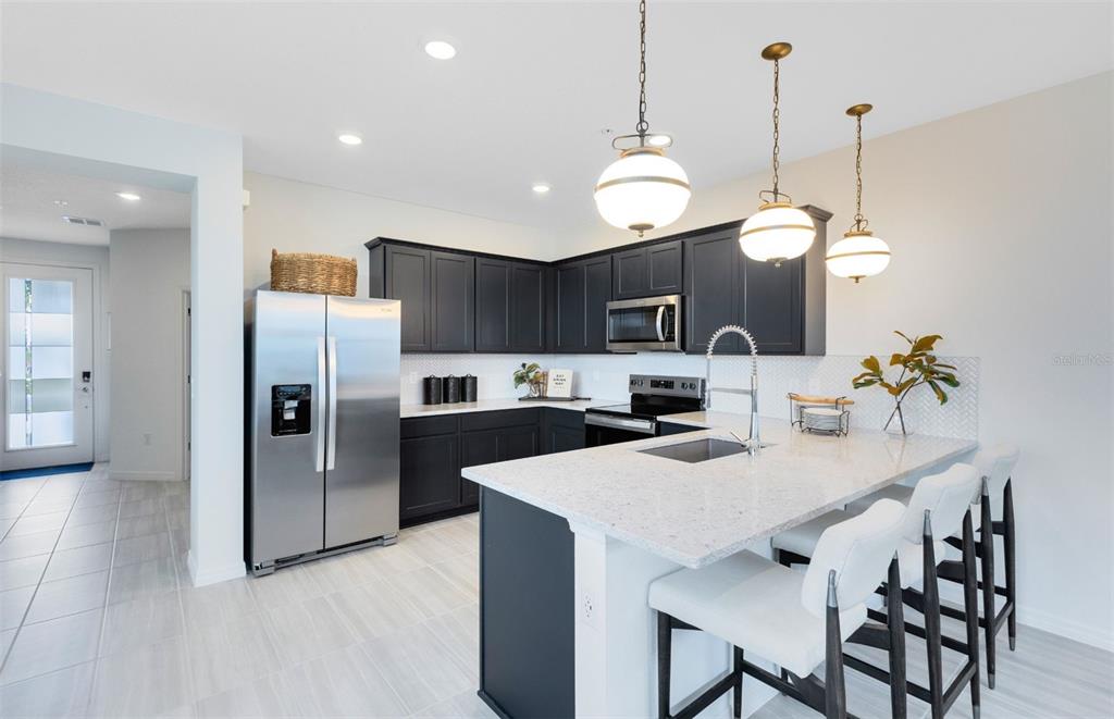 A modern kitchen features dark cabinets, stainless steel appliances, a quartz island, and three pendant lights — 1147 LEMONGRASS ALLEY, ORLANDO, FL
