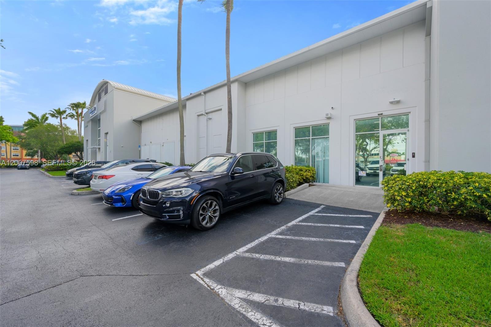 A dark SUV is parked in front of a white commercial building with glass doors — DORAL, FL