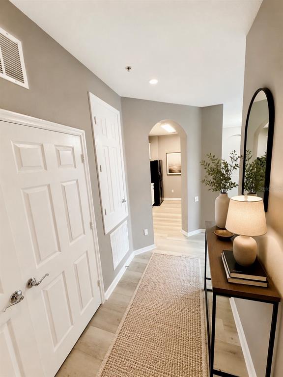 A hallway features light wood flooring, a console table with a lamp, and an arched entryway — 3332 ROBERT TRENT JONES DRIVE UNIT 20603, ORLANDO, FL