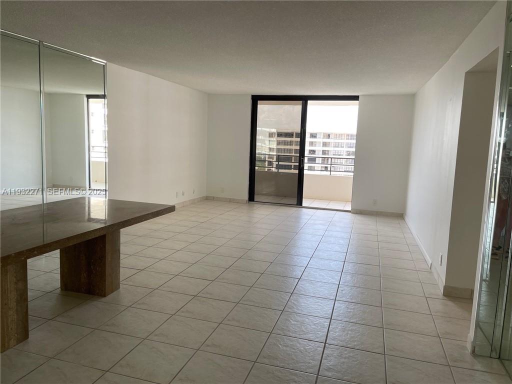 An empty living room features white tile floors, a mirrored wall, and a sliding glass door — 2500 Parkview Dr # 1920, Hallandale Beach FL 33009, HALLANDALE BEACH, FL