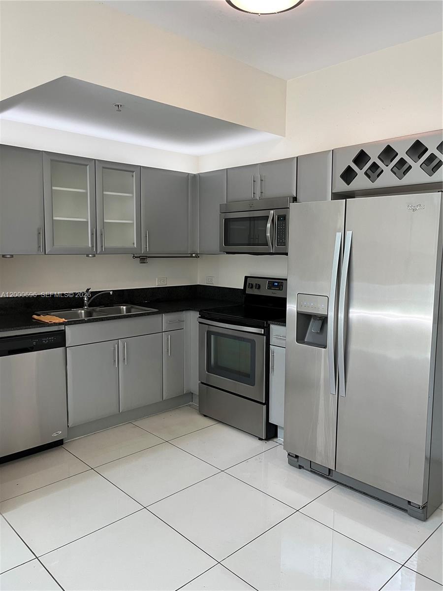 A kitchen features gray cabinets, stainless steel appliances, black countertops, and white tile flooring — 1871 NW S River Dr # A03, Miami FL 33125, MIAMI, FL