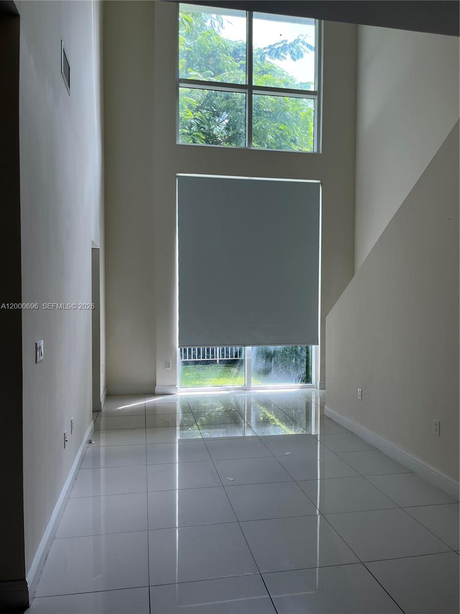 A bright, high-ceilinged room features white tile flooring, a large window, and a sliding door — 1871 NW S River Dr # A03, Miami FL 33125, MIAMI, FL