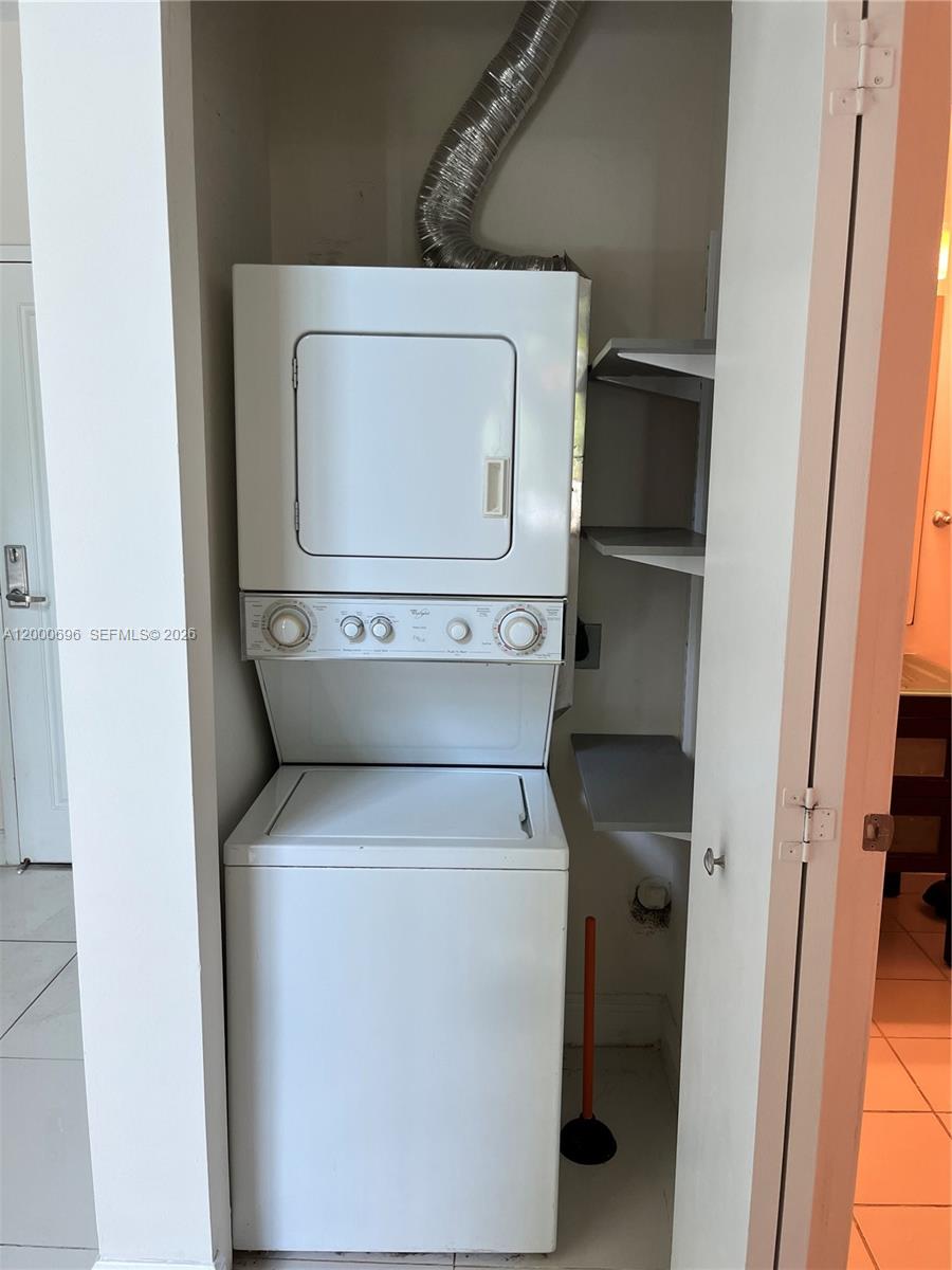 A stacked washer and dryer unit sits in a small closet with built-in shelving — 1871 NW S River Dr # A03, Miami FL 33125, MIAMI, FL