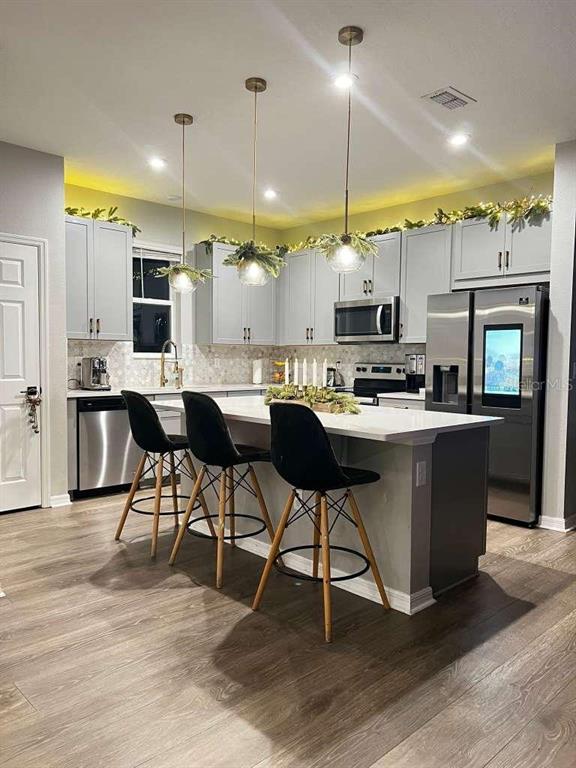 A modern kitchen features light gray cabinets, a central island with three stools, and pendant lighting — 9118 LONGSHIP ALLEY, ORLANDO, FL
