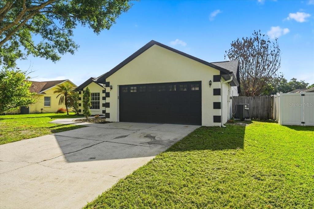 A single-story house with a yellow stucco exterior, black trim, and a two-car garage — 4209 RED BIRD AVENUE, ST CLOUD, FL