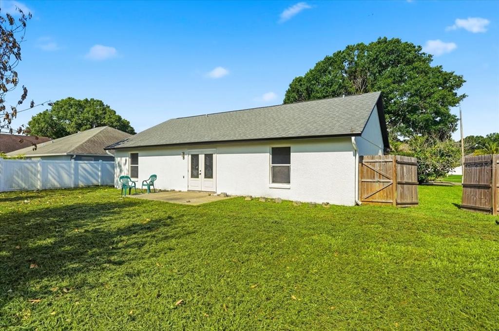 The backyard of a white house features a concrete patio, green lawn, and wooden fencing — 4209 RED BIRD AVENUE, ST CLOUD, FL