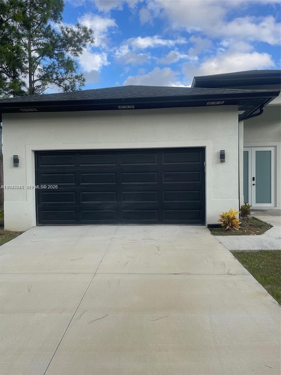 A white house exterior features a black two-car garage door and a glass-paneled front door — 321 S Briggs # 0, Lehigh Acres FL 33974, LEHIGH ACRES, FL