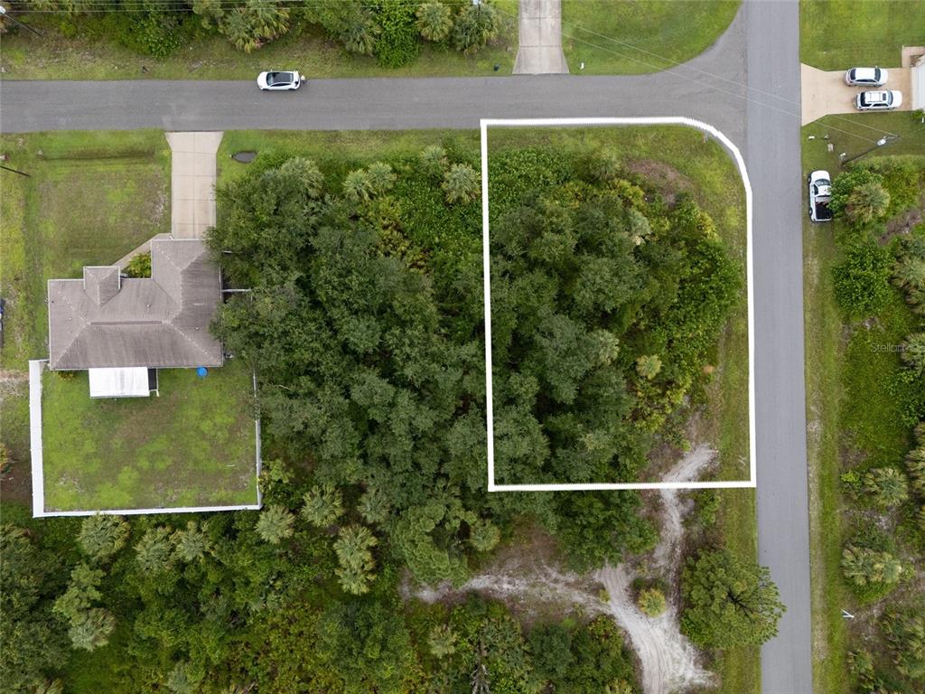 An aerial view shows a vacant, wooded corner lot outlined in white next to a house — BRONCO LANE, NORTH PORT, FL