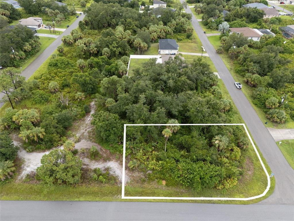 An aerial view shows a vacant, wooded corner lot outlined in white along paved streets — BRONCO LANE, NORTH PORT, FL