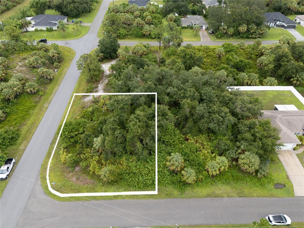 An aerial view shows a vacant, tree-covered residential lot outlined in white on a corner — BRONCO LANE, NORTH PORT, FL