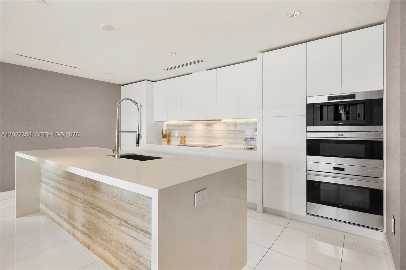 A modern kitchen features white cabinetry, a stone-accented island, and stainless steel built-in appliances — 102 24th St # 1718, Miami Beach FL 33139, MIAMI BEACH, FL