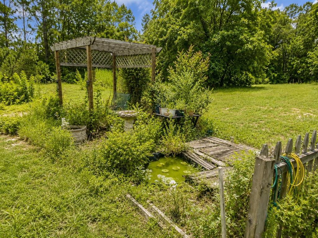 A wooden pergola stands over a small garden pond with a wooden deck and fence — 2221 DAFFODIL AVENUE, MIDDLEBURG, FL