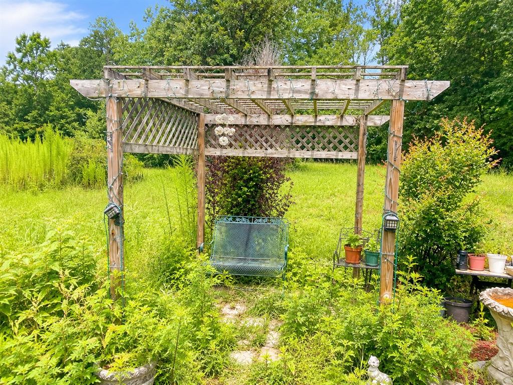 A wooden pergola stands in a grassy yard, featuring a metal bench and potted plants — 2221 DAFFODIL AVENUE, MIDDLEBURG, FL