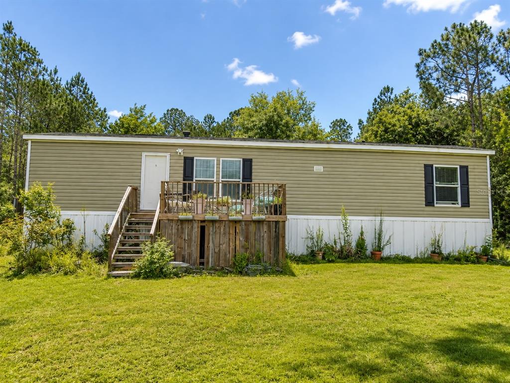 A single-story manufactured home with light green siding, a wooden deck, and a grassy yard — 2221 DAFFODIL AVENUE, MIDDLEBURG, FL