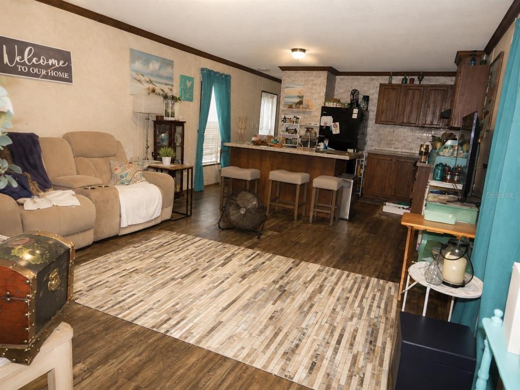 A living room with a beige sofa, wood-look flooring, and an open kitchen with bar seating — 2221 DAFFODIL AVENUE, MIDDLEBURG, FL