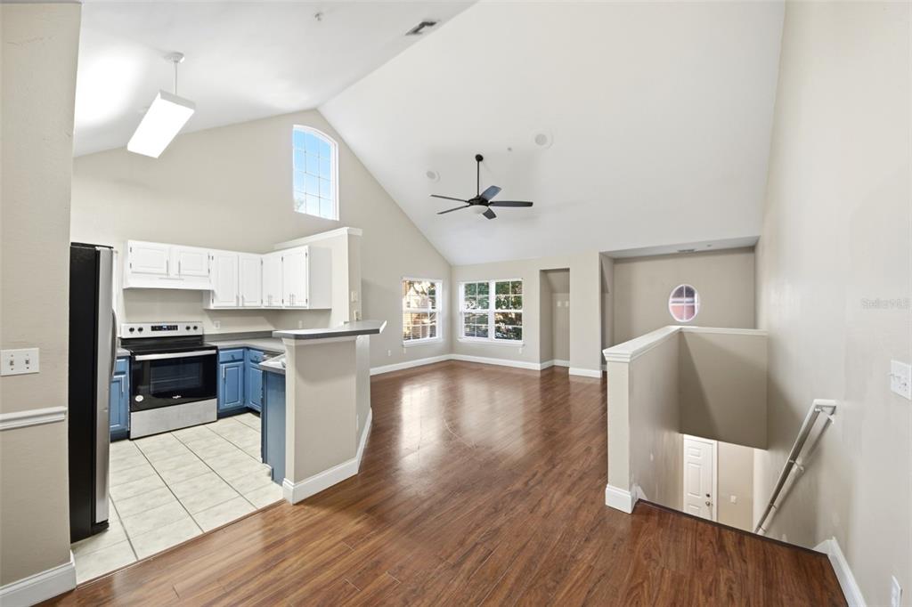 An open-concept kitchen and living area with vaulted ceilings, wood flooring, and blue cabinetry — 3364 WESTCHESTER SQUARE BOULEVARD UNIT 202, ORLANDO, FL