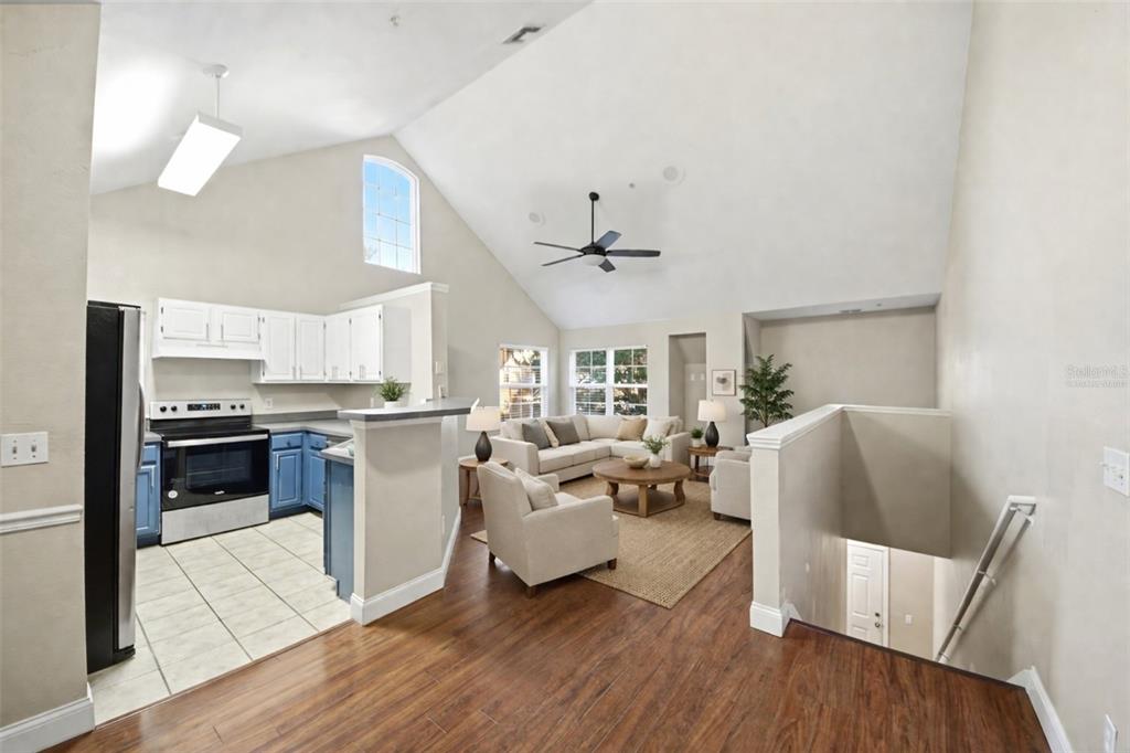 An open-concept living room and kitchen with vaulted ceilings, wood flooring, and neutral walls — 3364 WESTCHESTER SQUARE BOULEVARD UNIT 202, ORLANDO, FL