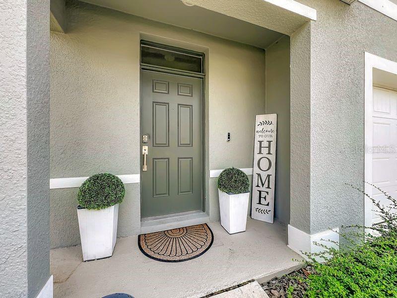 A front entryway features a green door, two potted topiary plants, and a welcome sign — 1157 CASCADES AVENUE, DAVENPORT, FL