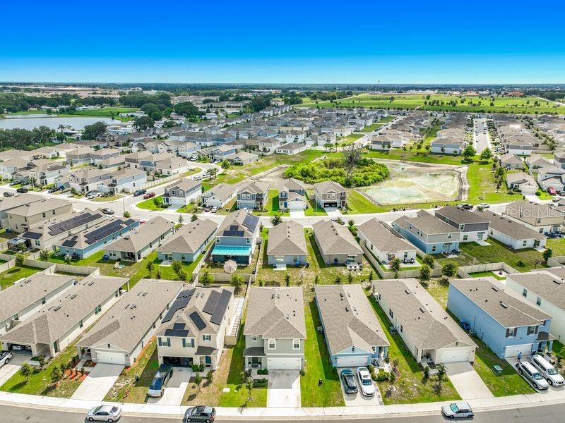An aerial view shows a suburban neighborhood with numerous single-family homes and a central pond — 1157 CASCADES AVENUE, DAVENPORT, FL