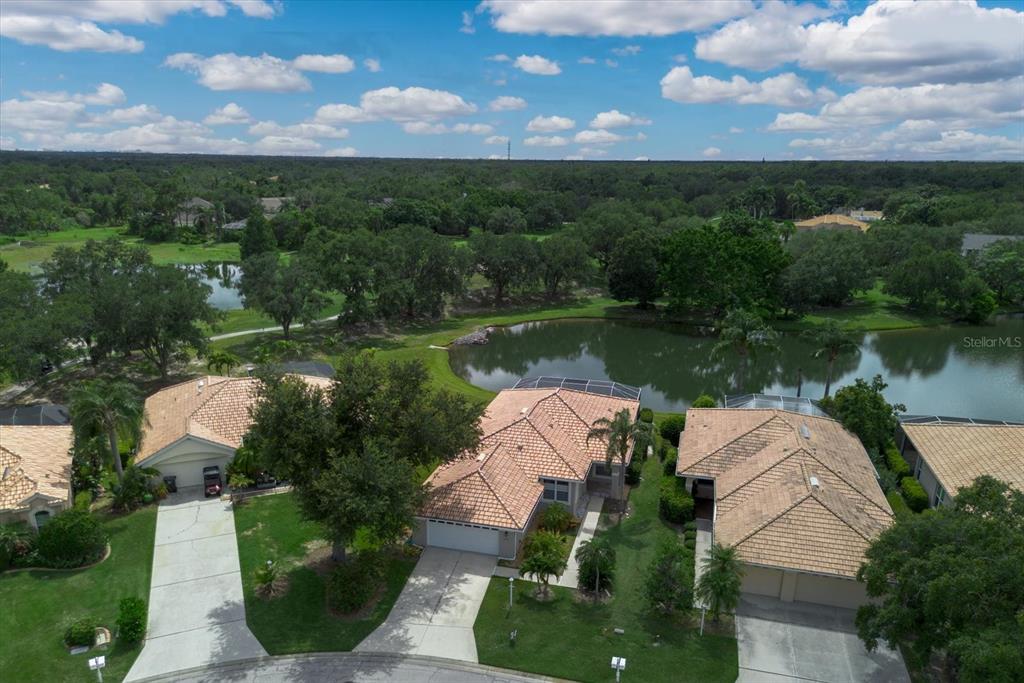 An aerial view shows three suburban houses with tile roofs situated near a small lake — 6726 HICKORY HAMMOCK CIRCLE, BRADENTON, FL