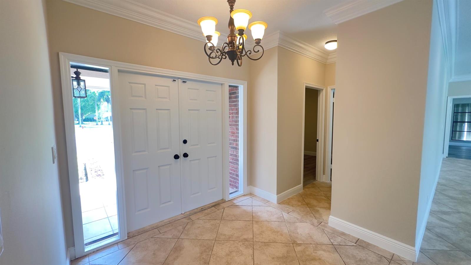 An entryway features a double door, tile flooring, a chandelier, and a brick sidelight — 11330 Timberlodge Terrace, Boca Raton FL 33428, BOCA RATON, FL