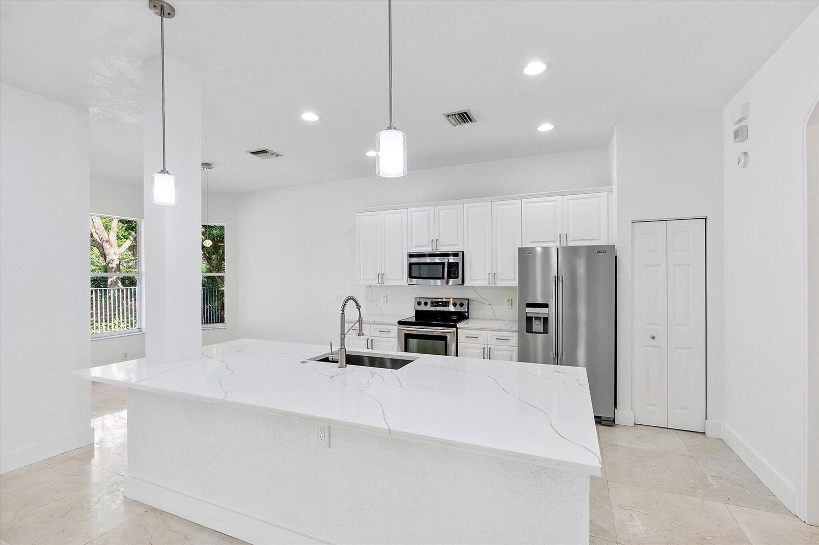 A modern kitchen features white cabinets, stainless steel appliances, and a large marble-topped island — 2013 Harbor View Circle, Weston FL 33327, WESTON, FL