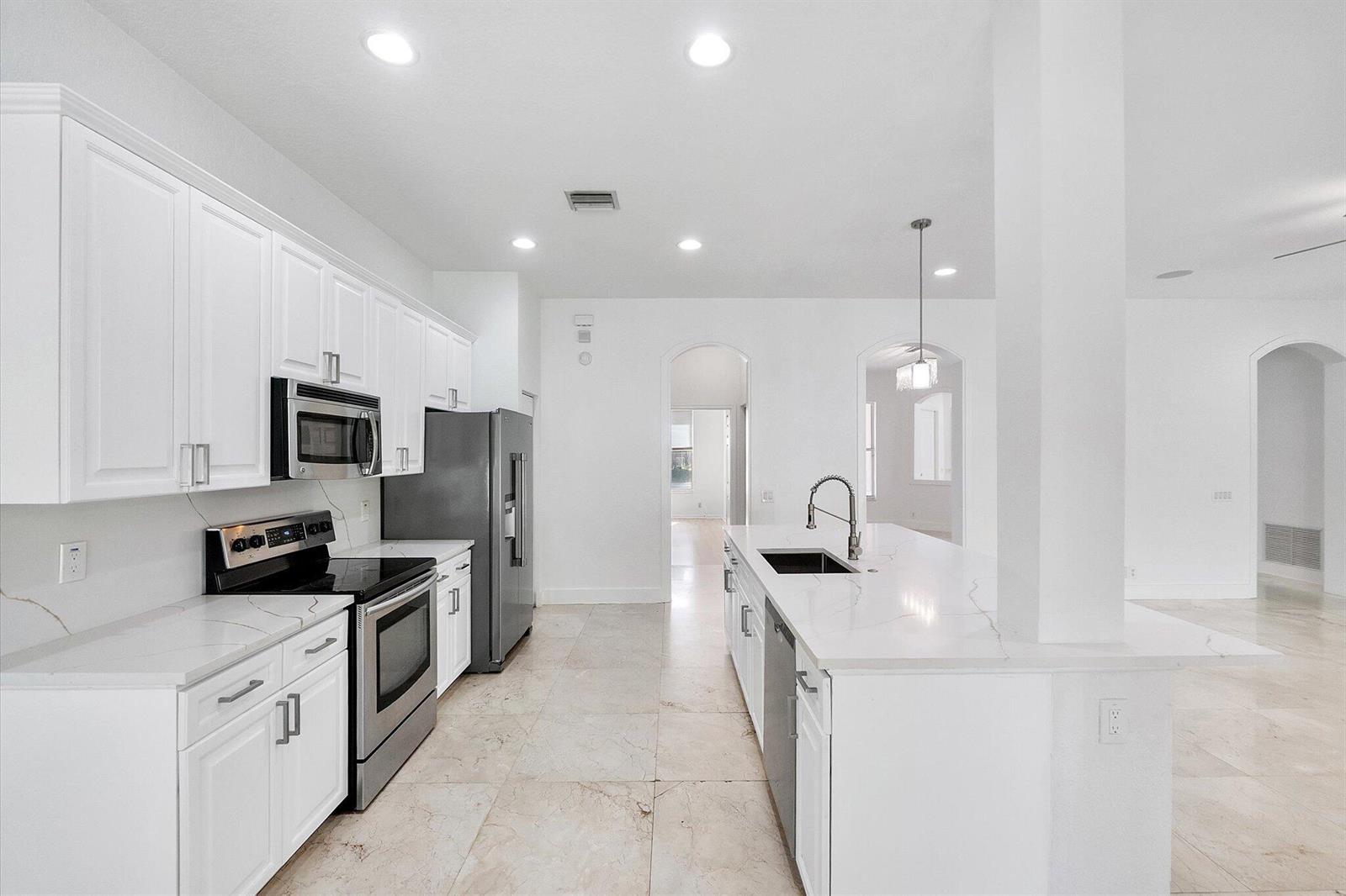 A modern kitchen features white cabinetry, stainless steel appliances, and a large marble-topped island — 2013 Harbor View Circle, Weston FL 33327, WESTON, FL