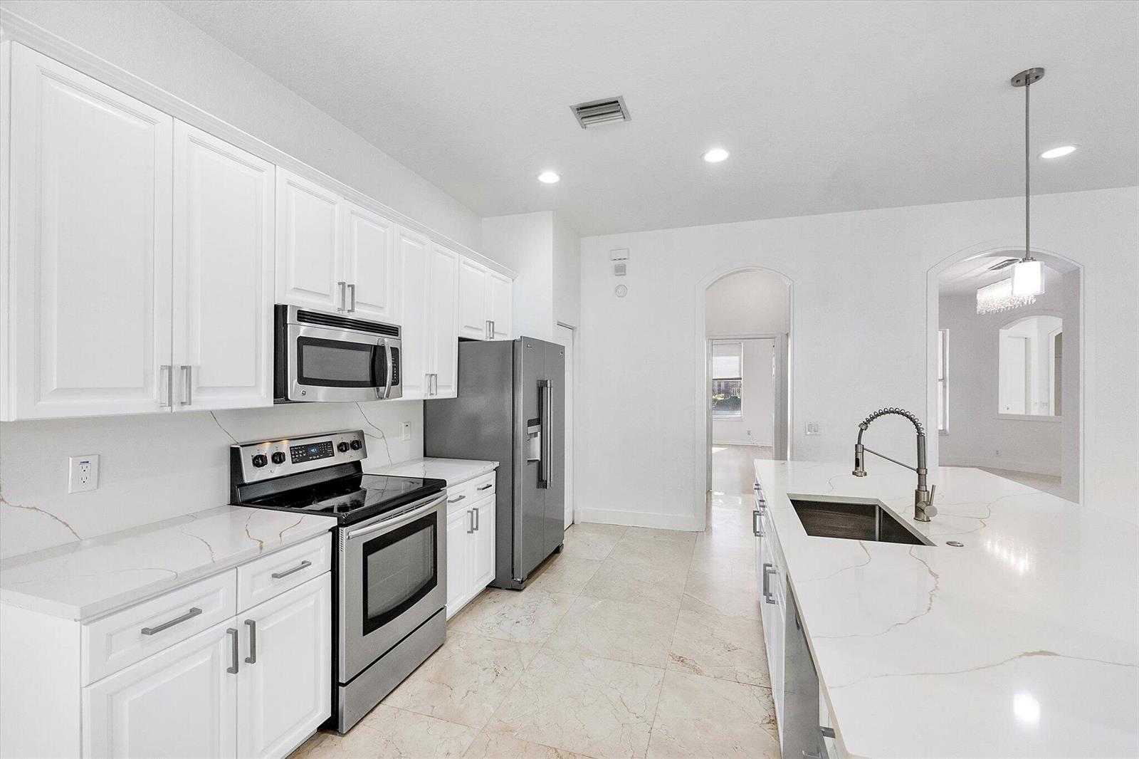 A modern kitchen features white cabinets, stainless steel appliances, and a large quartz-topped island — 2013 Harbor View Circle, Weston FL 33327, WESTON, FL