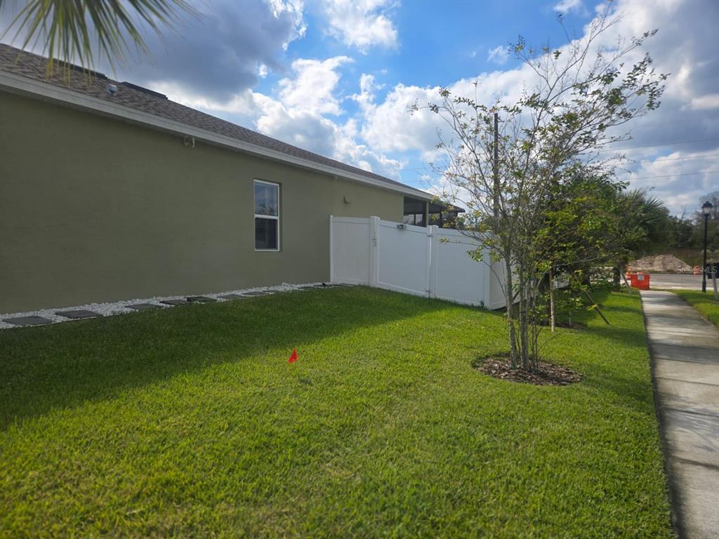 A side view of a house exterior with a white vinyl fence and green lawn — 8052 GREENWAY AVENUE, WESLEY CHAPEL, FL